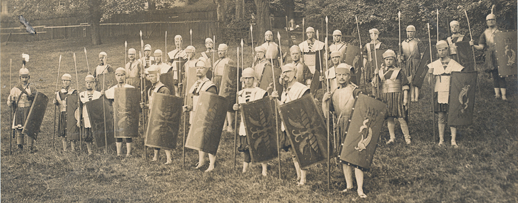 black and white photo of a group of people dressed as roman soldiers, posing in front of some trees.